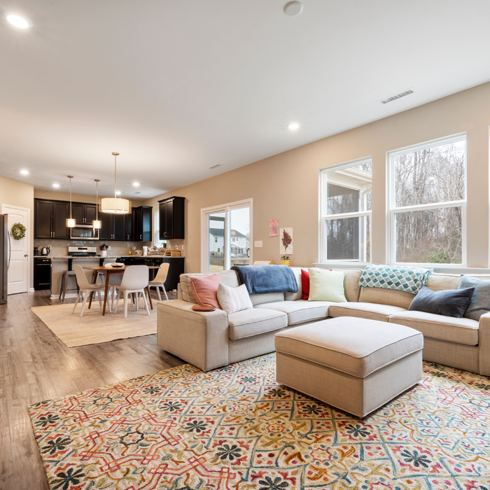 contemporary styled living room with a white couch, ornate style area rug and the kitchen in the background