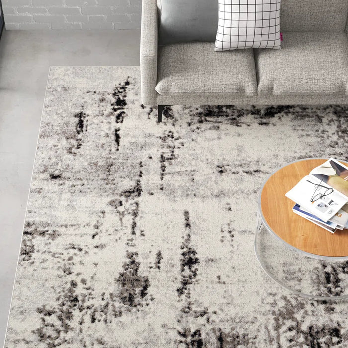 Top view of a modern living room with a gray couch, a round coffee table with books, and the Ceslie Gray/Charcoal Area Rug.