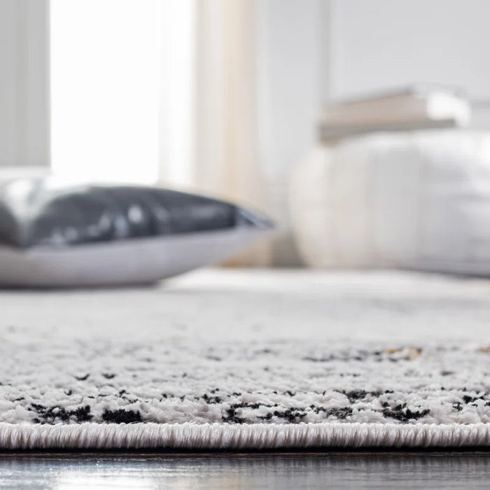 Close-up view of a living room featuring the soft, light-colored Acosta Rug, with a blurred gray pillow on the floor and out-of-focus furniture in the background.
