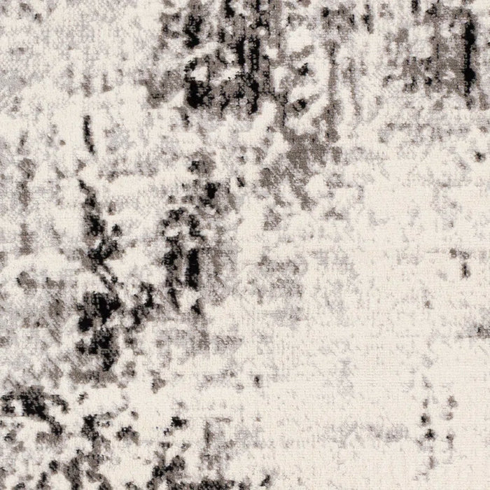 A close-up view of the textured surface of the Ceslie Gray/Charcoal Area Rug, featuring an abstract, black and white pattern resembling irregular smudges and brush strokes.