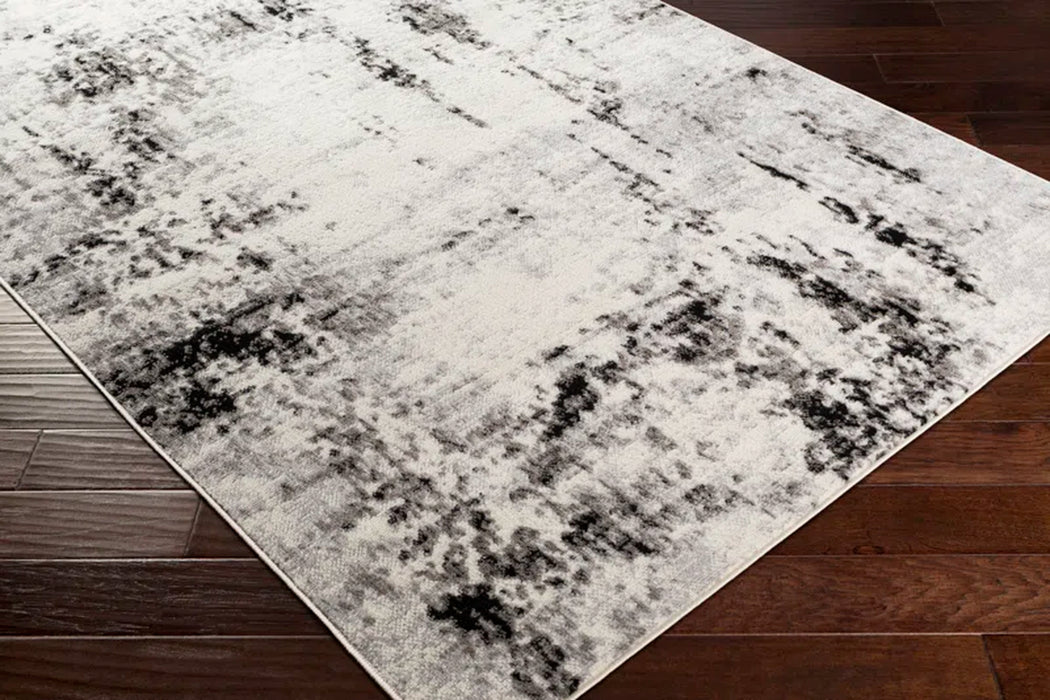 A close-up of the Ceslie Gray/Charcoal Area Rug featuring a white, grey, and black abstract pattern displayed on a dark wooden floor.