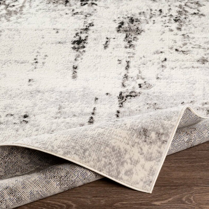 A close-up of the Ceslie Gray/Charcoal Area Rug with a corner lifted, revealing the underside, on a wooden floor.