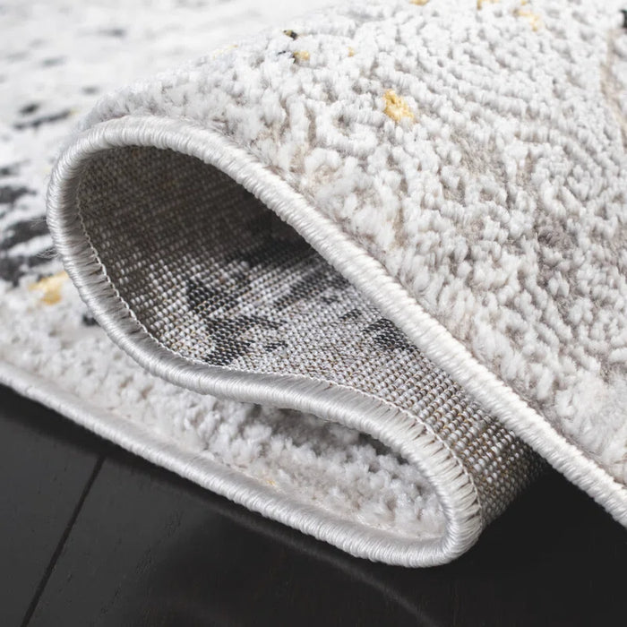 Close-up view of the corner of the Acosta Rug, rolled up to showcase its intricate gray and white textured patterns, placed on a dark wooden floor.