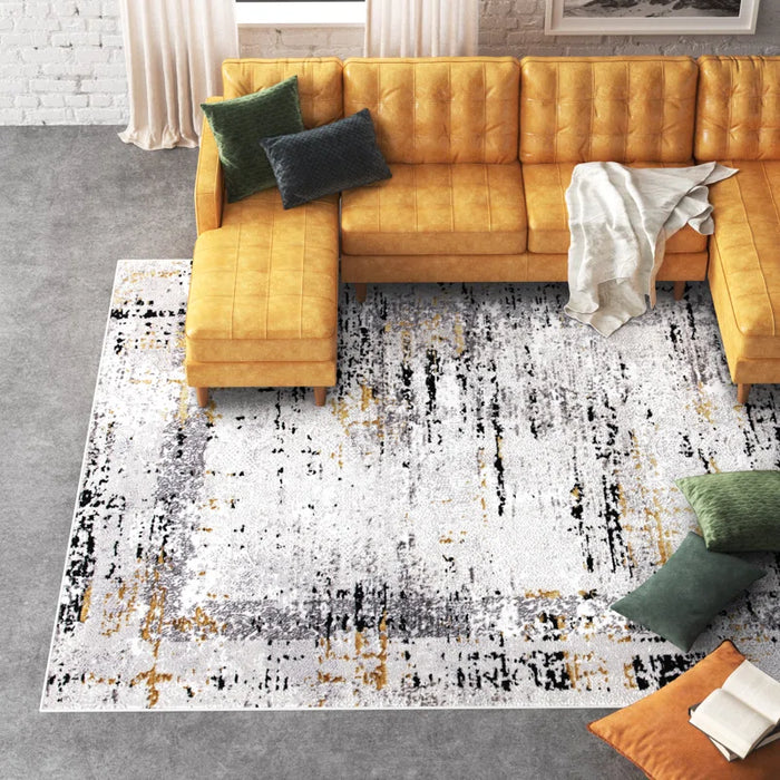 A mustard yellow L-shaped sofa with green and gray pillows sits on an Acosta Rug, featuring a textured white, gray, and yellow pattern, in a bright living room.