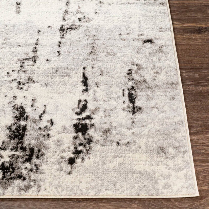 Close-up of a corner of the Ceslie Gray/Charcoal Area Rug featuring abstract black patterns on a dark wood floor background.