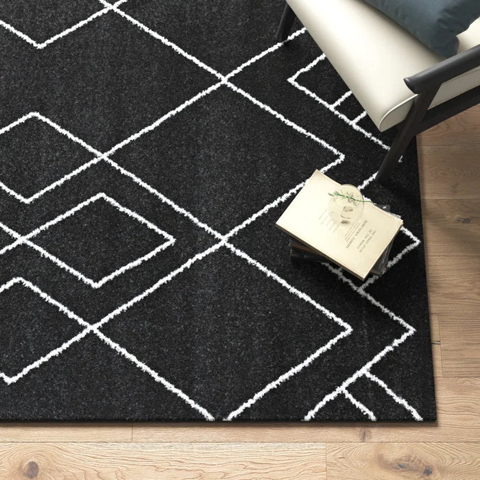Dedham Geometric Black Area Rug laid out on a wooden floor, accompanied by a chair and books on the rug.
