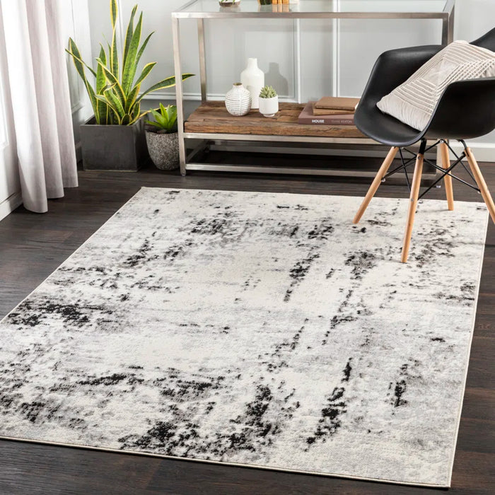 A modern living room features the Ceslie Gray/Charcoal Area Rug, a black chair with wooden legs, plants, and decorative items on a metal console table.