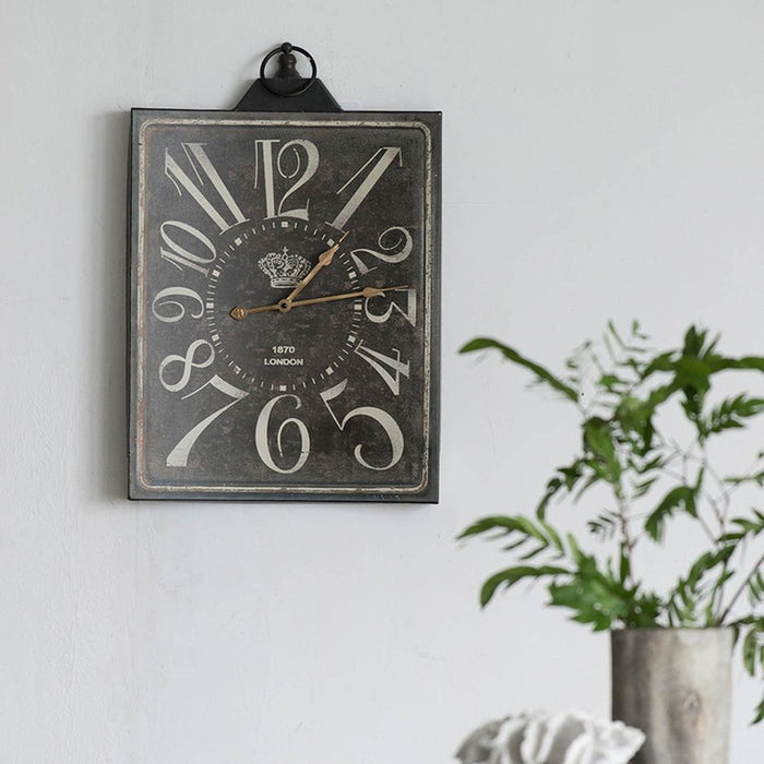 Vintage-style wall clock on a white wall with a plant in the foreground