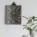 Vintage-style wall clock on a white wall with a plant in the foreground