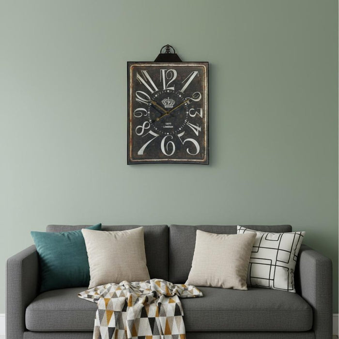 Decorative wall clock on a green wall above a gray sofa with cushions.