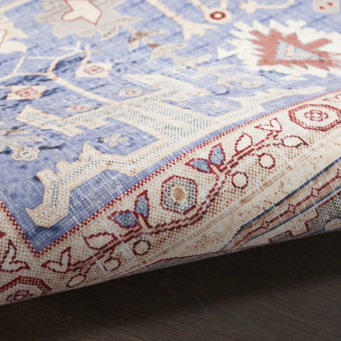 Close-up of a patterned rug with blue, red, and beige colors on a wooden floor.