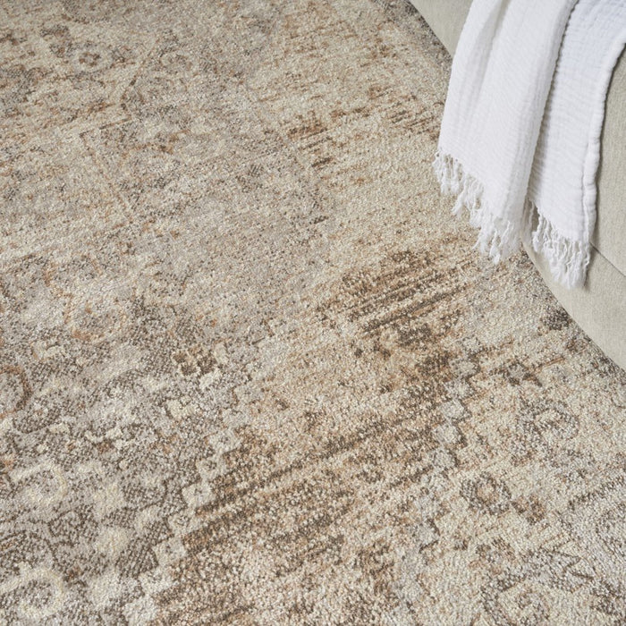 Close-up of a textured beige and brown area rug with a white blanket corner.