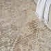 Close-up of a textured beige and brown area rug with a white blanket corner.