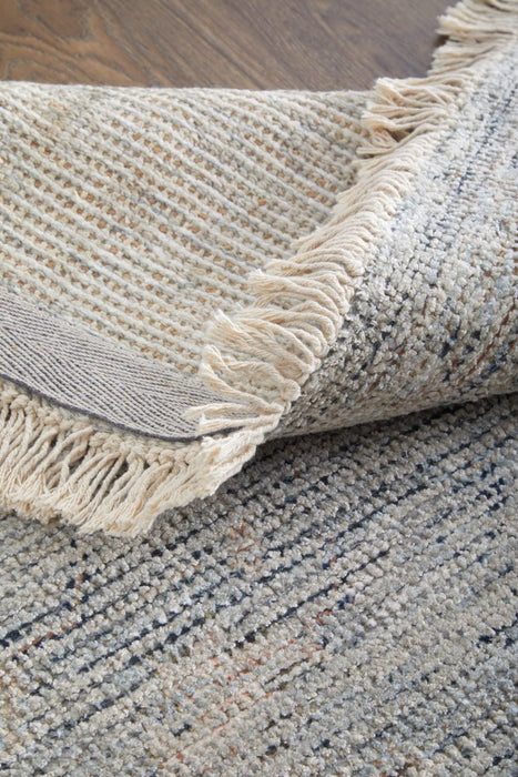 Close-up of textured area rugs with fringe on a wooden floor.