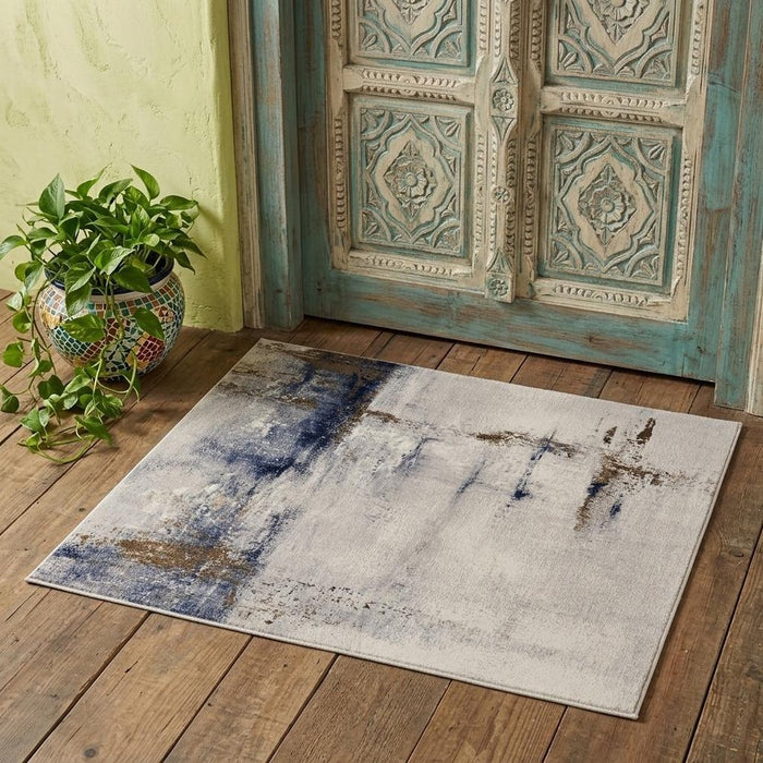 Abstract patterned rug on a wooden floor with a decorative wooden door and plant in the background.