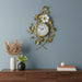 Decorative wall clock with floral design on a blue wall above a wooden shelf with plants and books.
