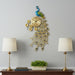 Decorative peacock wall clock on a wall with two lamps and a plant below.