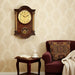 Decorative wall clock on a wall above a small table with a book and cup, next to a maroon armchair with a patterned pillow.