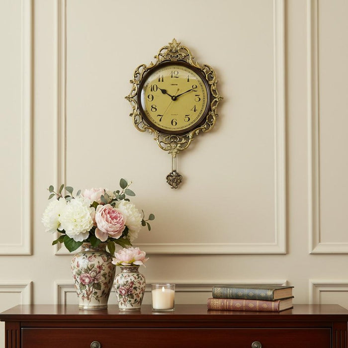 Decorative wall clock with floral arrangements and books on a wooden cabinet against a beige wall.