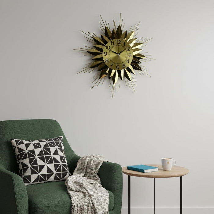 Gold sunburst clock on a white wall above a green armchair with a geometric pillow.