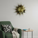 Gold sunburst clock on a white wall above a green armchair with a geometric pillow.
