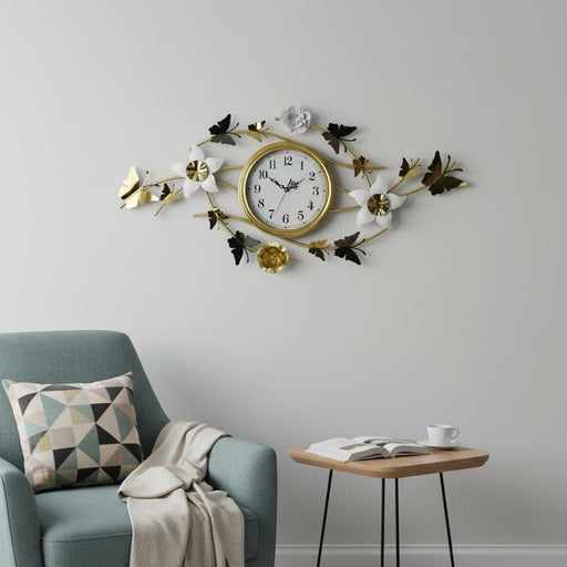 Decorative wall clock with floral and butterfly design on a gray wall above a blue armchair.