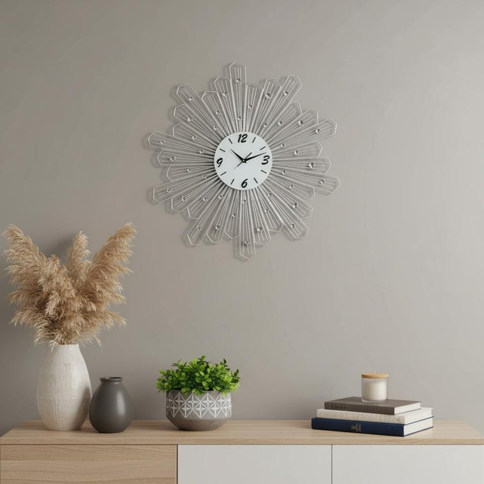 Decorative wall clock on a gray wall with a wooden shelf featuring vases and plants.