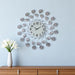 Decorative wall clock with floral design on a light blue wall, next to a wooden cabinet and white vase with flowers.