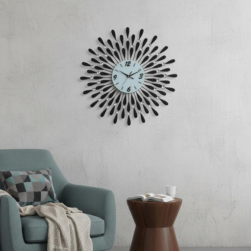 Decorative wall clock with black feather-like design on a gray wall above a sofa.