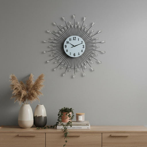 Decorative wall clock with a starburst design on a gray wall above a wooden cabinet with decorative items.