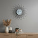 Decorative wall clock with a starburst design on a gray wall above a wooden cabinet with decorative items.