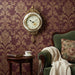 Decorative wall clock on a patterned wall with a chair and small table below.