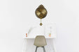 Decorative wall clock with a pendulum on a white wall above a table with a chair.