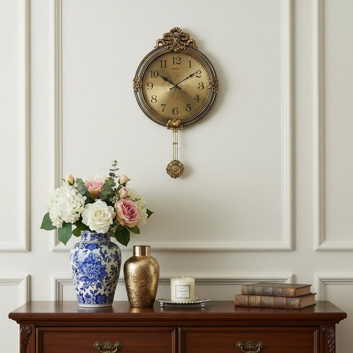 Decorative wall clock with floral arrangement and books on a wooden cabinet against a white paneled wall.