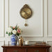 Decorative wall clock with floral arrangement and books on a wooden cabinet against a white paneled wall.