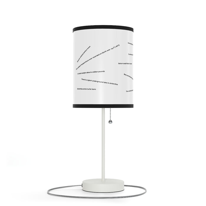 The Random Fact Table Lamp is modern, with a cylindrical shade, abstract text, and a pull chain on a circular base.