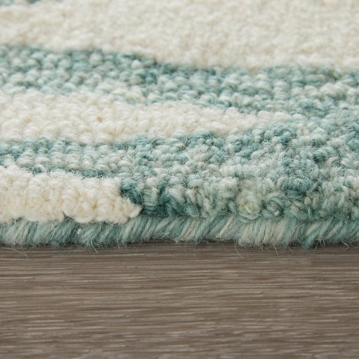 Close-up of a textured rug with green and beige stripes on a wooden floor.