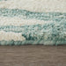 Close-up of a textured rug with green and beige stripes on a wooden floor.