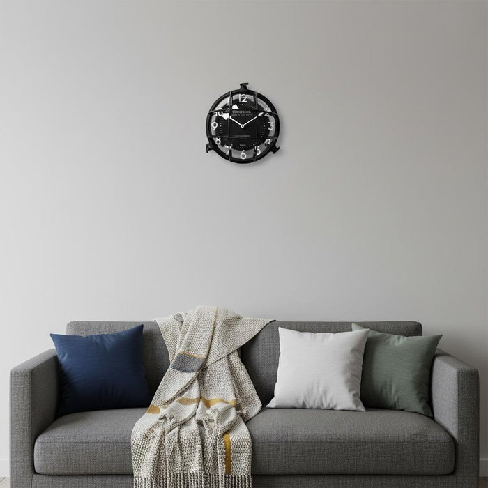 Wall clock on a gray wall above a gray sofa with cushions and a blanket.